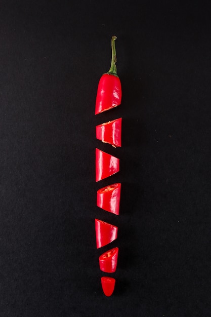 Бесплатное фото Свежий красный перец нарезать ломтиками на черной поверхности