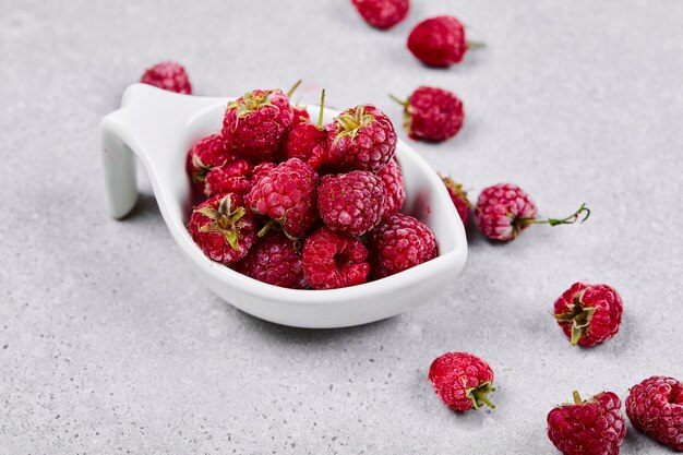 Fresh red raspberries in white bowl on white surface.