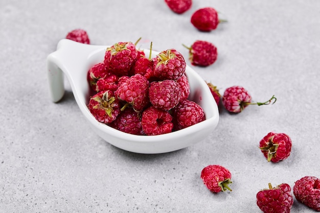 Fresh red raspberries in white bowl on white surface.