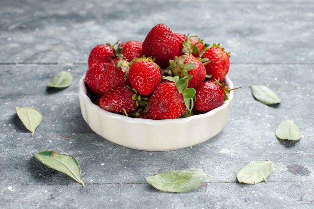 fresh red strawberries inside white plate along with green dried leaves on grey desk, fruit fresh berry color photo vitamine health