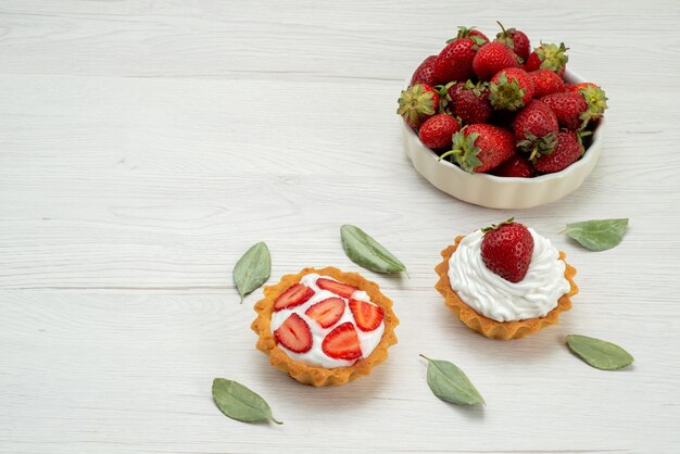 свежая красная клубника, спелая и вкусные ягоды на белой тарелке с пирожными на свете