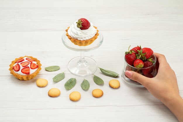 fresh red strawberries mellow and delicious berries with cakes and cookies on light grey desk