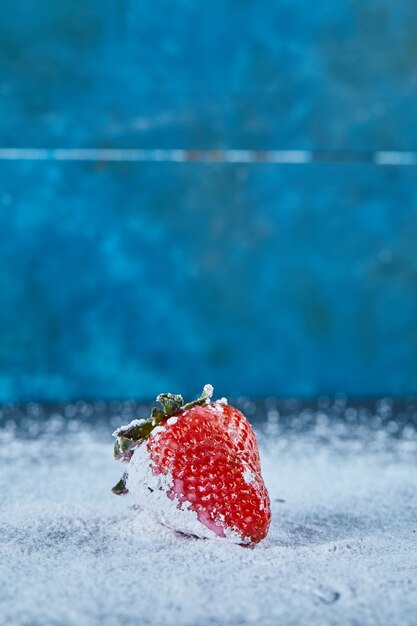 Fresh red strawberry on blue surface with powder