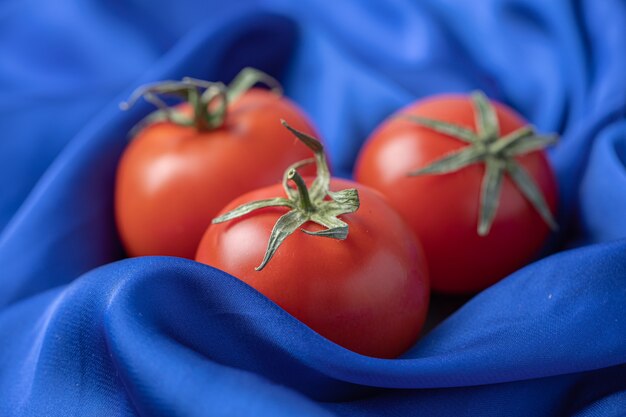 Fresh red tomatoes on blue tablecloth .
