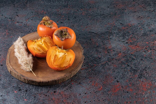 Fresh ripe persimmons with wheat ear placed on a wooden piece