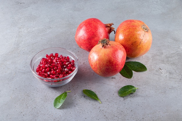 Free photo fresh ripe pomegranates with bowl of seeds placed on stone table.