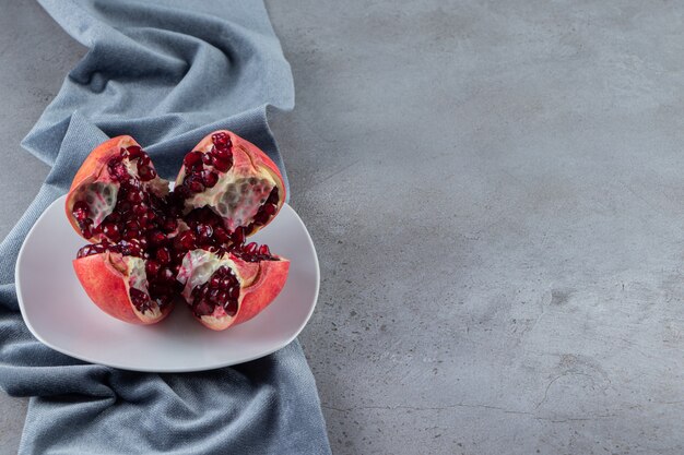 Fresh ripe pomegranates with seeds placed on white plate. 