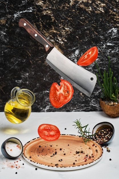 Free photo fresh ripe tomatoes are cut with a knife and dropped onto plate with rosemary, salt, pepper and olive oil