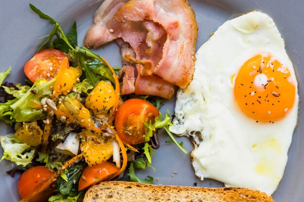 Fresh salad; bacon; half fried eggs and toast on gray plate