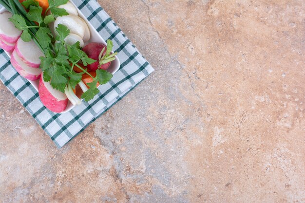 Fresh salad ingredients bundle on a platter on a folded towel on marble surface