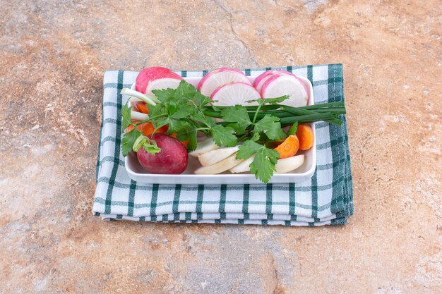 Fresh salad ingredients bundle on a platter on a folded towel on marble surface