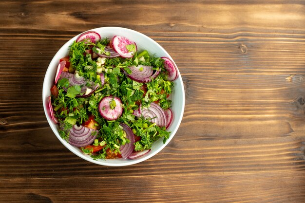 Бесплатное фото Свежий салат, богатый витаминами, с красной луковой редькой и помидорами внутри с зеленью сверху на деревянной деревенской поверхности