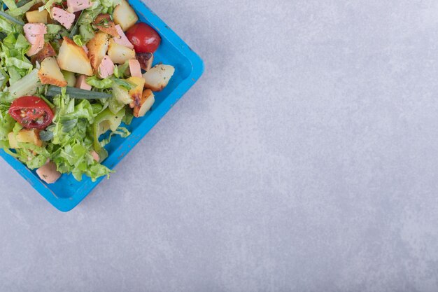 青いプレートに茹でたソーセージを添えたフレッシュサラダ。