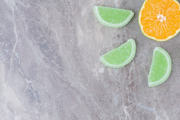 Fresh slice of orange with sweet marmalades on marble background.