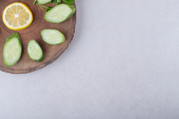 Fresh, sliced cucumber, lemon and parsley on a board, on the marble.