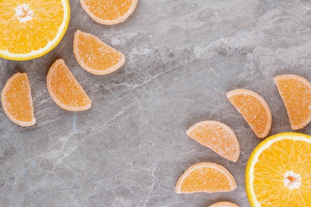 Свежие дольки апельсина со сладким мармеладом на мраморном фоне.