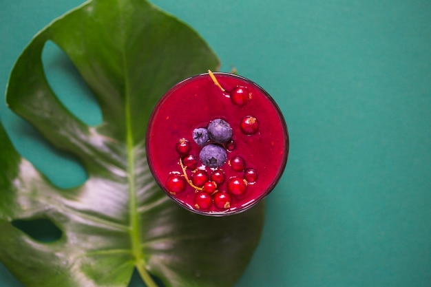 Fresh smoothie glass on monstera leaf over the green background