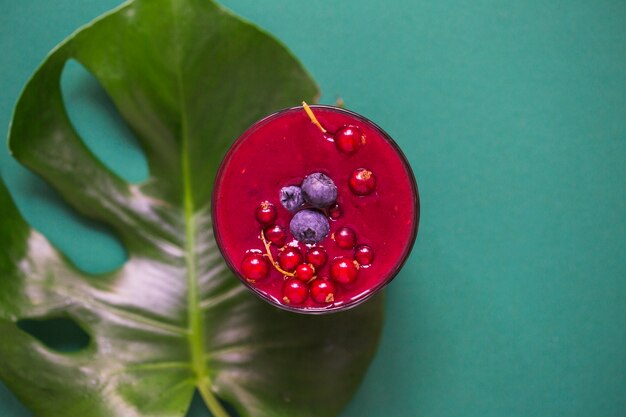 Fresh smoothie glass on monstera leaf over the green background