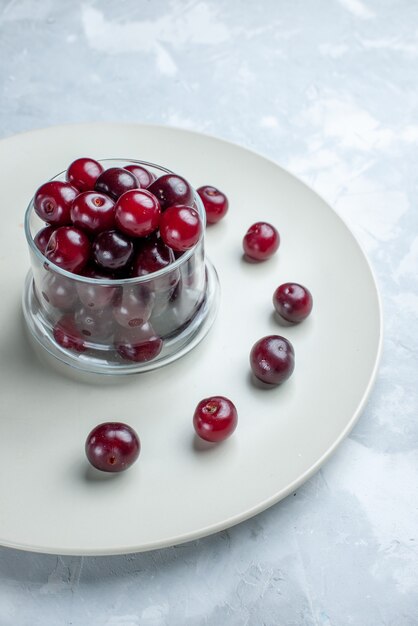 fresh sour cherries inside plate on light white desk, fruit sour berry vitamine summer