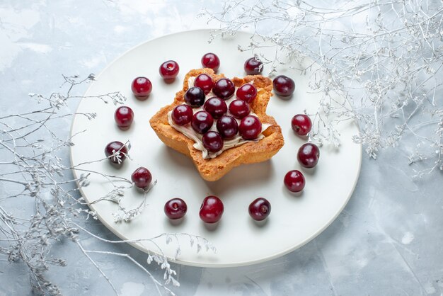свежая вишня внутри тарелки со сливочным пирогом в форме звезды на сером