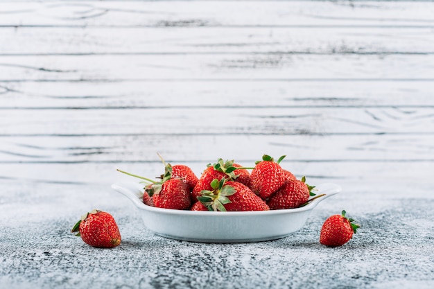 Fresh strawberries in a dish on a light grey stucco background. side view.