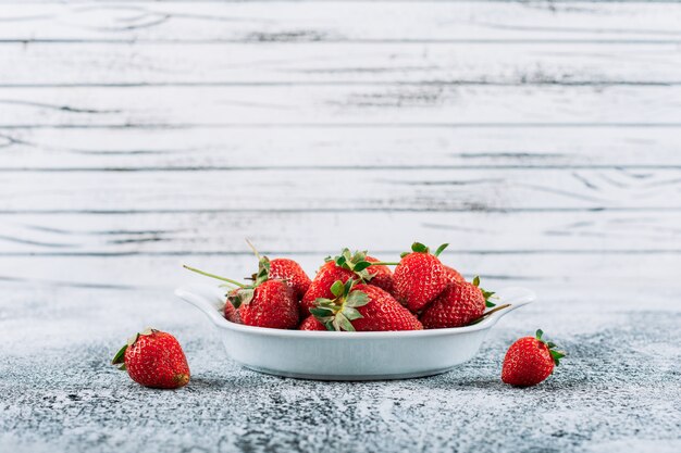 Fresh strawberries in a dish on a light grey stucco background. side view.