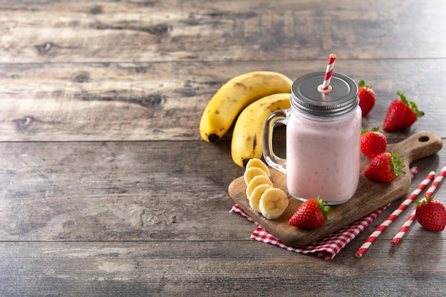 Fresh strawberry and banana smoothie in jar on wooden table