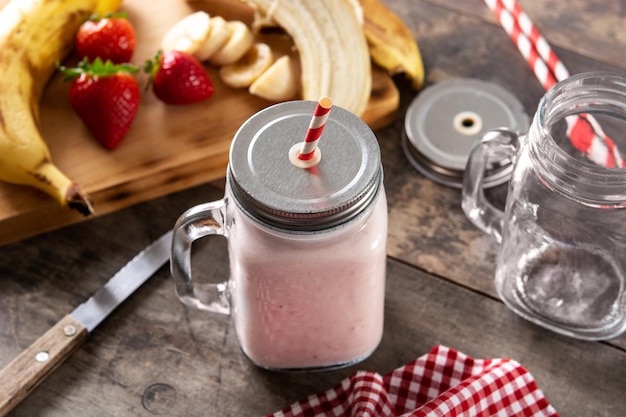 Fresh strawberry and banana smoothie in jar on wooden table