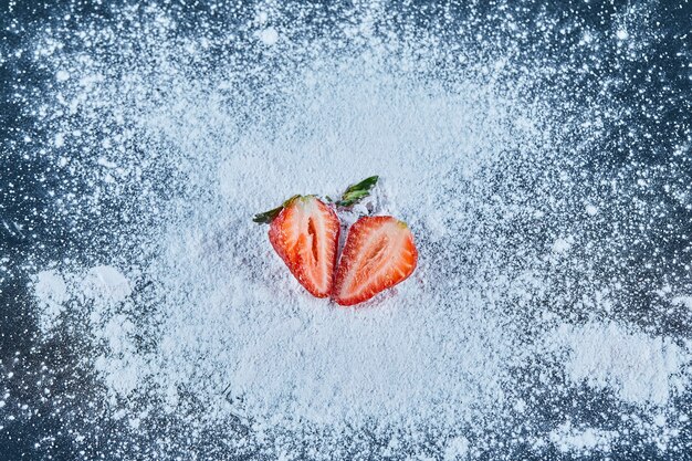 Fresh strawberry slices on blue surface with powder