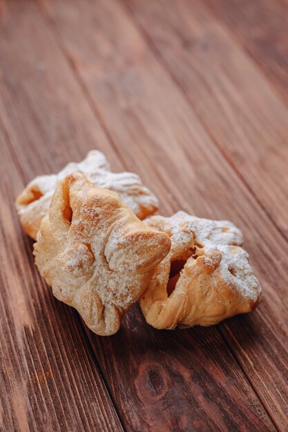 A fresh sweet pastry is sprinkled with sugar powder on a wooden surface