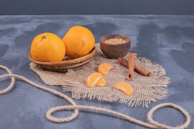 Fresh tangerines in bowl and cinnamon on blue surface.