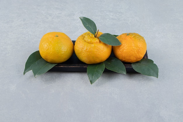 Fresh tangerines with leaves on black plate. 