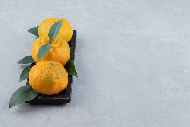 Fresh tangerines with leaves on black plate