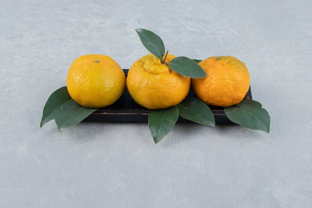 Бесплатное фото Свежие мандарины с листьями на черной тарелке.