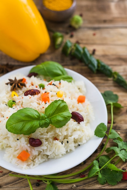Свежий вкусный вегетарианский рис на тарелке с листьями базилика и петрушкой