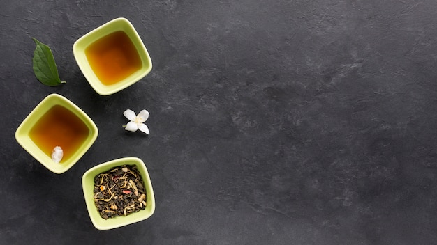 Free photo fresh tea with dried herb and jasmine flower on black surface