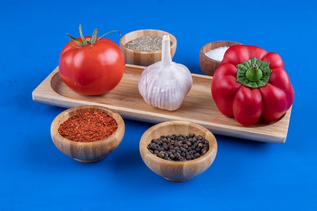 Free photo fresh tomato, garlic and red bell pepper on wooden plate.