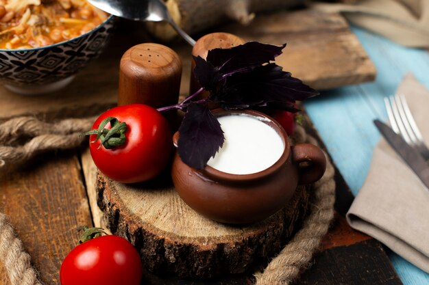 Fresh tomatoes, basilic and a pot of yogurt on the wooden board.