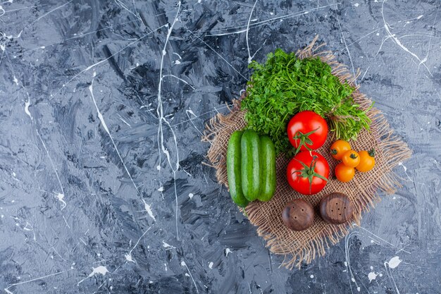 Fresh tomatoes, cucumbers and parsley leaves on marble surface.