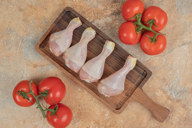 Foto gratuita pomodori freschi con tavola di legno di cosce di pollo crude