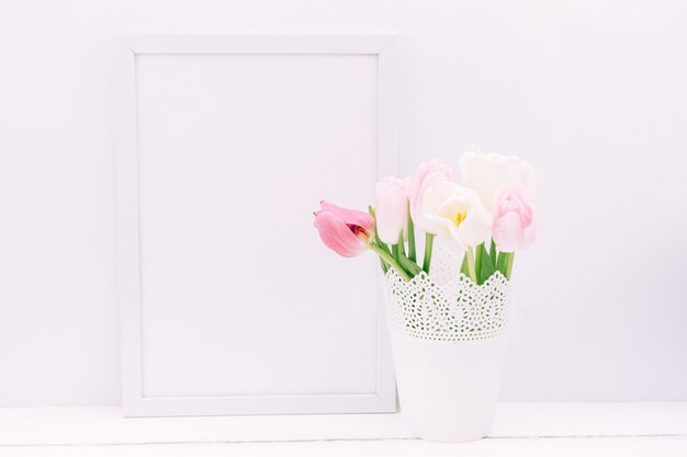 Fresh tulip flowers in vase with blank photo frame