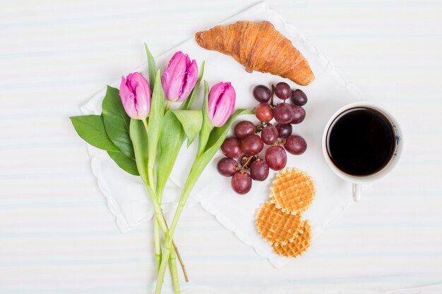 Fresh tulips; croissant; grape fruits; waffles and tea cup on white background