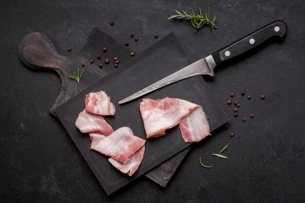 Fresh uncooked bacon on wooden board with knife