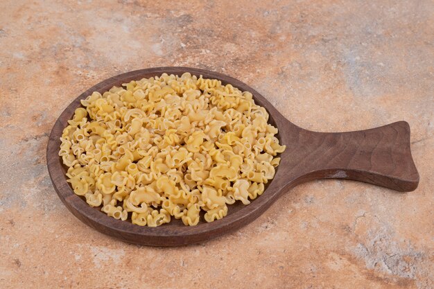 Fresh uncooked macaroni on wooden board on marble background