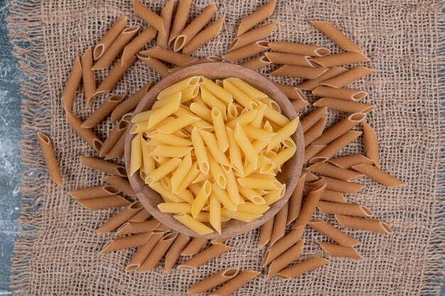 Fresh uncooked macaroni on wooden bowl on burlap. High quality photo