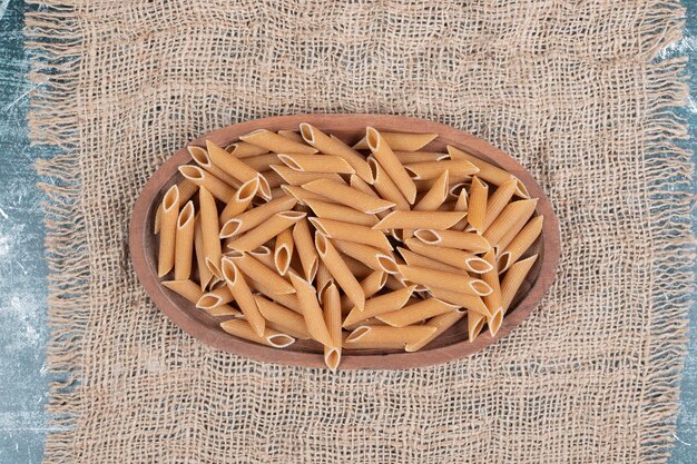 Fresh uncooked macaroni on wooden bowl on burlap. 