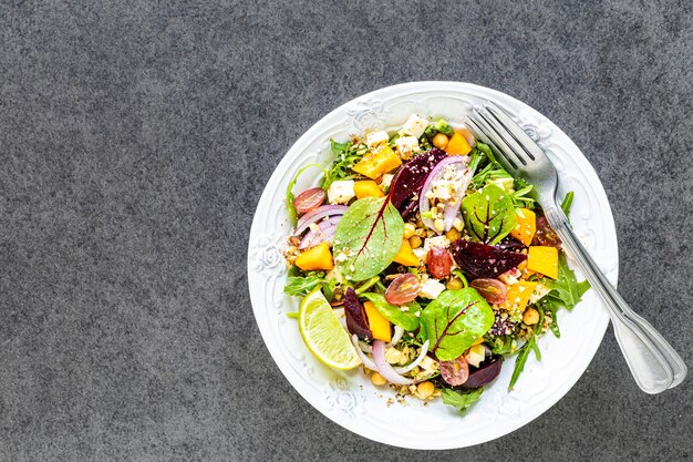 Fresh vegetable salad with beetroot, arugula, red onion, sorrel, chickpeas, pumpkin and grapes in a white plate on black. Top view