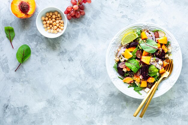 사탕 무우 arugula 붉은 양파 밤색 병아리 콩 복숭아와 흰색 돌 배경 상위 뷰에 흰색 접시에 포도와 신선한 야채 샐러드