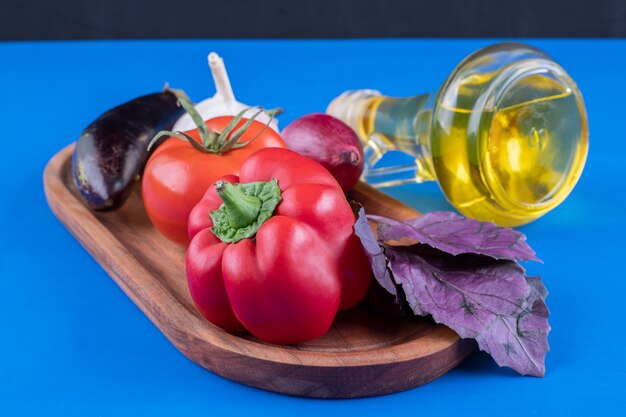 Свежие овощи и бутылка оливкового масла на деревянной тарелке