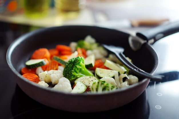 Приготовление свежих овощей на сковороде на домашней кухне. Крупный план.